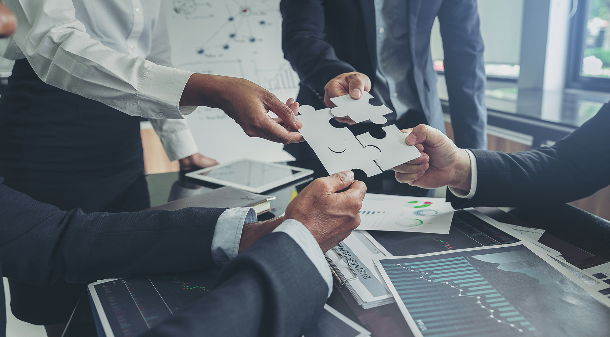 Quatre personnes dont on ne voit que les mains, possèdent chacune une partie d'un puzzle, qu'elles essaient de réunir dans un bureau. Une image qui illustre bien l'article "pourquoi est-il important de se créer un réseau professionnel" pour le blog de trouve ton emploi.